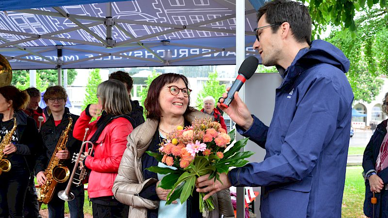 Übergabe eines Blumenstraußes bei der Eröffnungsfeier des Colombini-Spielplatzes, begleitet von einer Bläsergruppe